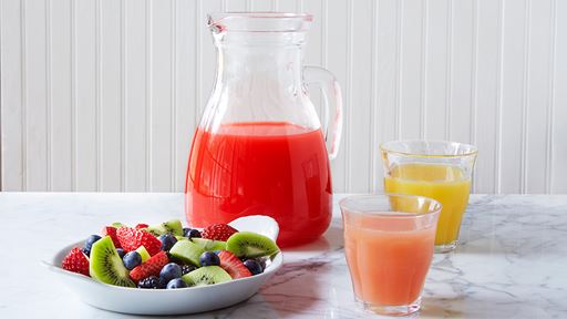 Freshly squeezed juice in a pitcher next to sliced fruit and two poured glasses of juice.
