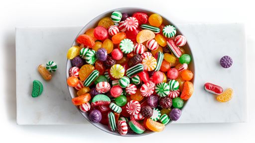 Wooden bowl overflowing with variety of hard candy on clean white plate.