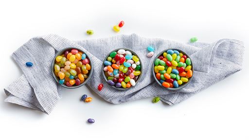 Three round ramekins filled with different soft candies and jelly beans spaced evenly on top of a blue napkin on a white background.