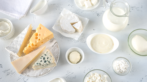 Variety of hard and soft cheeses in different simple white dishes on a white wood table top.