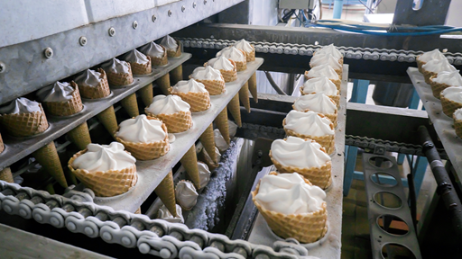 Commercial machinery filling up waffle cones with soft serve ice cream. 