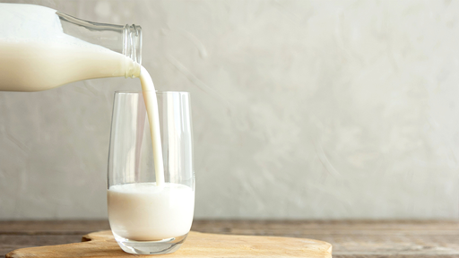 A fresh bottle of milk being poured smoothly into a glass on a wood table with a white background. 