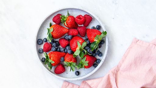 Strawberries and blueberries on a circular dish sat on top of a light salmon colored napkin.