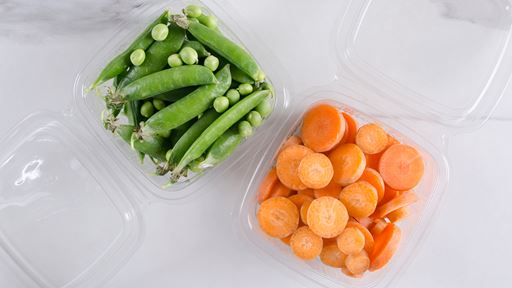 Two clear containers, one filled with peas the other filled with sliced carrots positioned in the middle of the image with a white background.