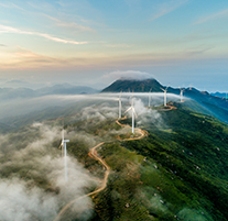 Aerial shot of wind turbines by windy road on cloudy mountaintop. 