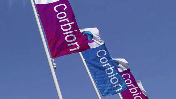 Corbion logoed flags blowing in blue sky. 