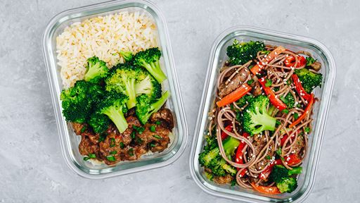 Two different freshly prepared meals in clear containers, one made of beef rice and broccoli the other of noodles peppers and broccoli.