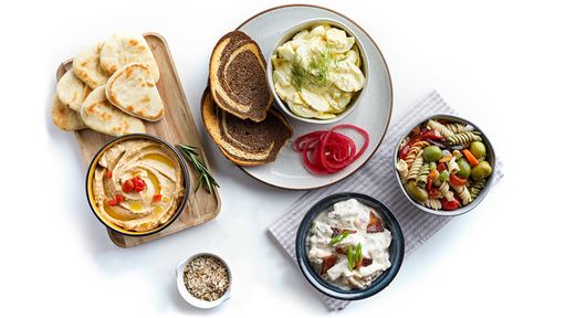 A wide spread of dishes each plated individually such as hummus and naan bread, potato salad and pasta salad.