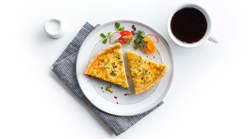 A freshly prepared and sliced quiche served on a simple circular white plate with coffee on the side.