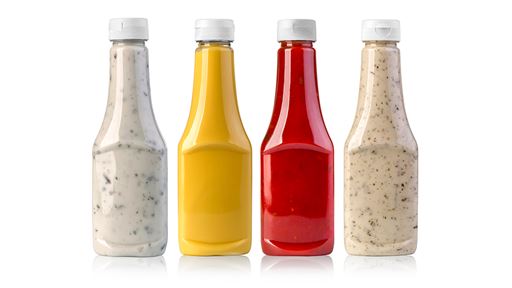 Four different clear bottles of different condiments and sauces lined up on a white background.