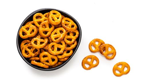 A black circular bowl filled with small crunchy salted pretzel snacks with a few off to the side of the bowl.