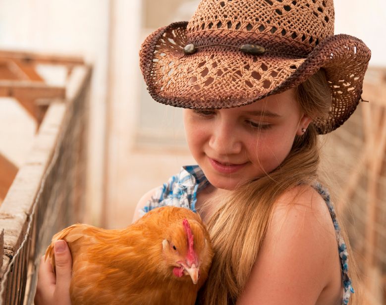 Girl in cowboy hat holding chicken. 