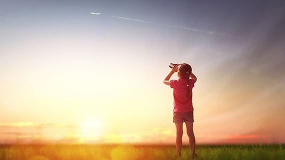 Girl looking through binoculars to the sky and flying plane.