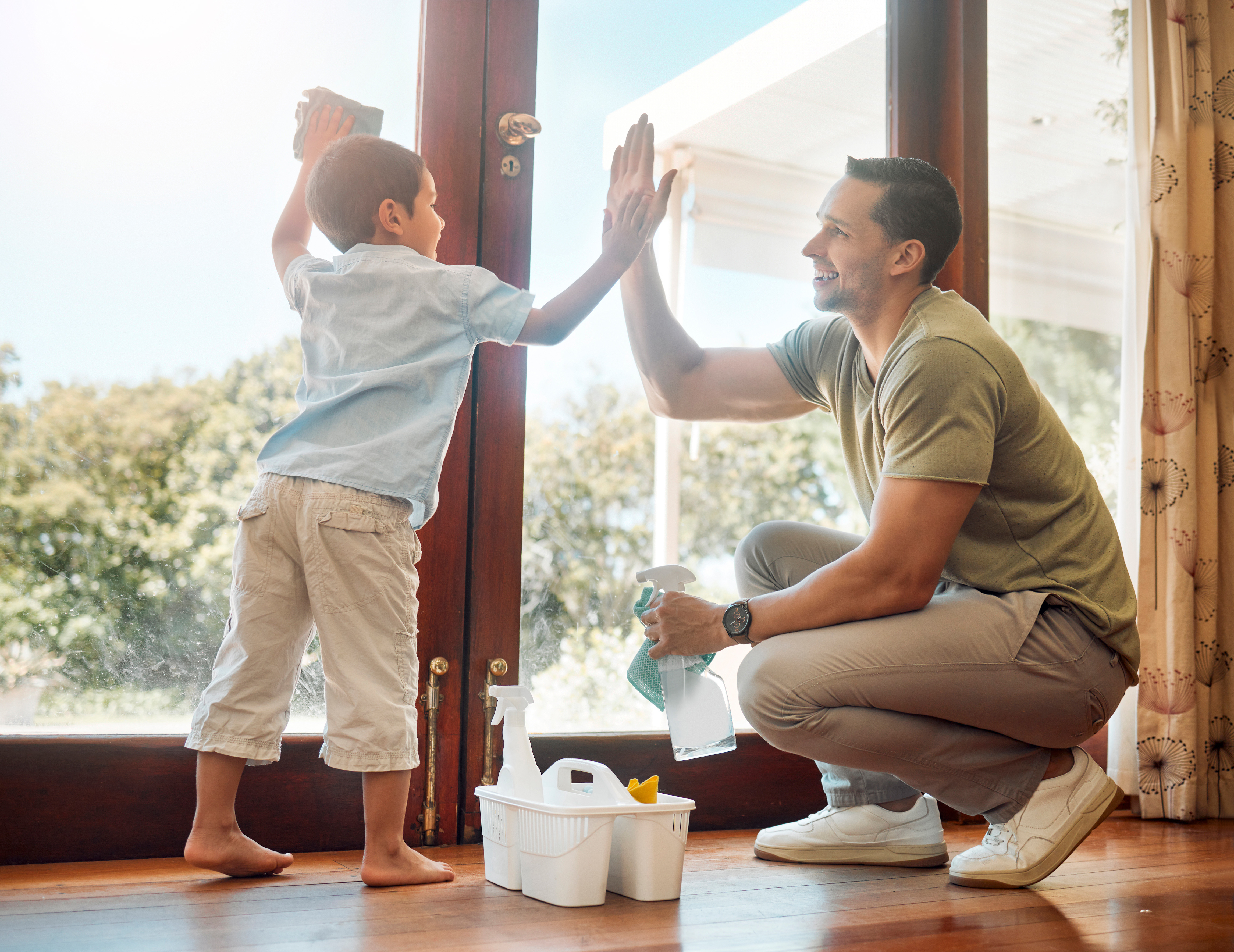Boy and father high fiving while cleaning glass door.