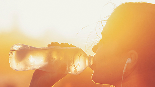 Woman with earbuds in sunlight drinking bottled water.