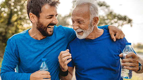 Adult father and son laughing while holding water bottles. 