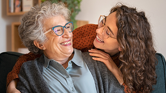 Elderly woman being embraced and smiling at younger woman.