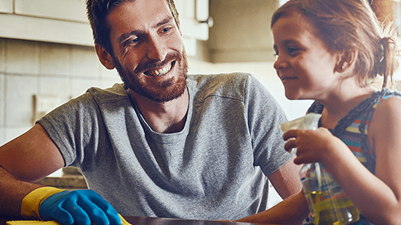 Smiling father and daughter with spray bottle cleaning kitchen counter.