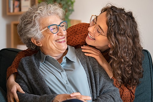 Elderly woman being embraced and smiling at younger woman.