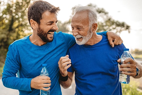 Adult father and son laughing while holding water bottles. 