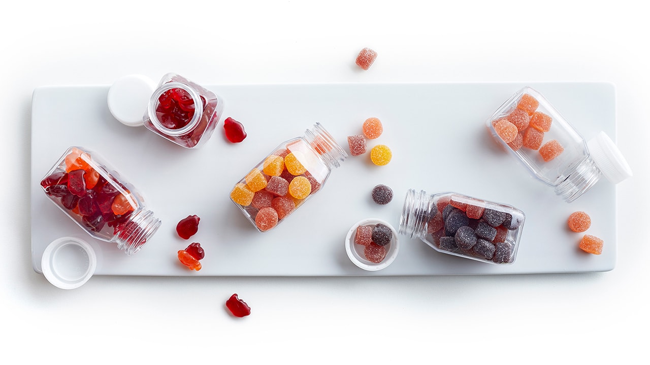 Vitamin gummies pouring from four different containers on to a white plate.
