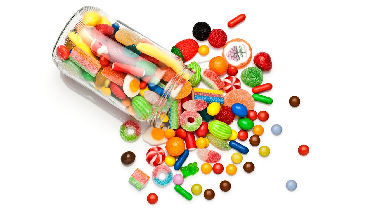 Large jar of different candy types poured out on a white background.