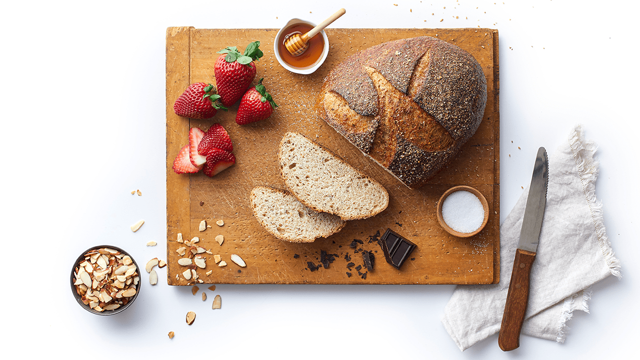 Loaf of bread partially sliced on cutting board with strawberries. 
