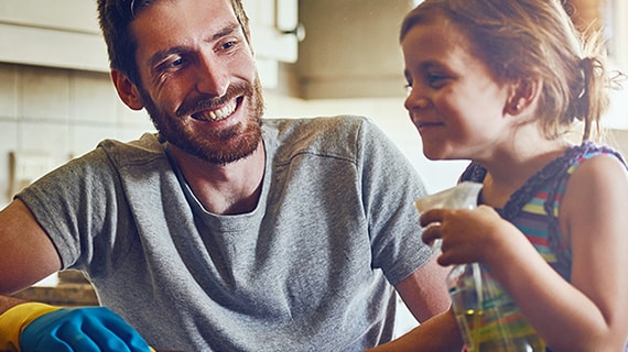 Smiling father and daughter with spray bottle cleaning kitchen counter.