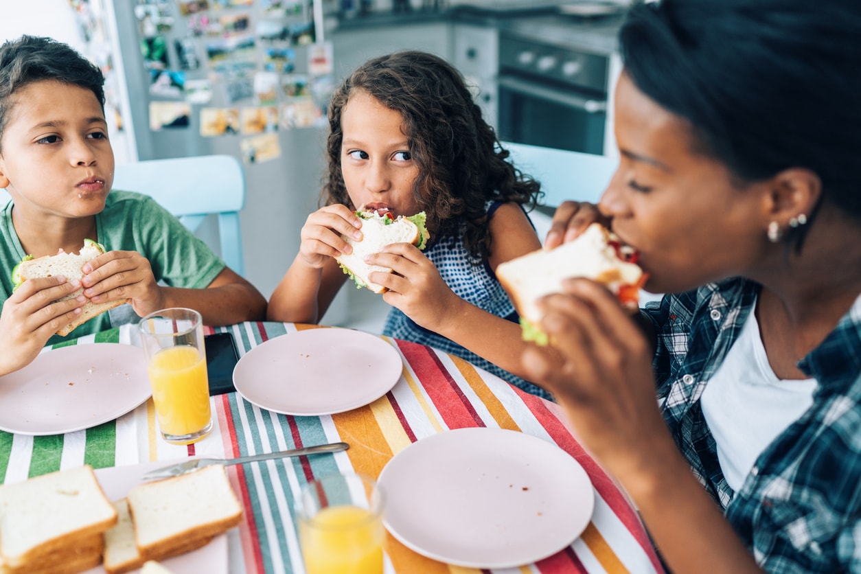 Modern mother with her two children eating sandwiches in the kitchen.