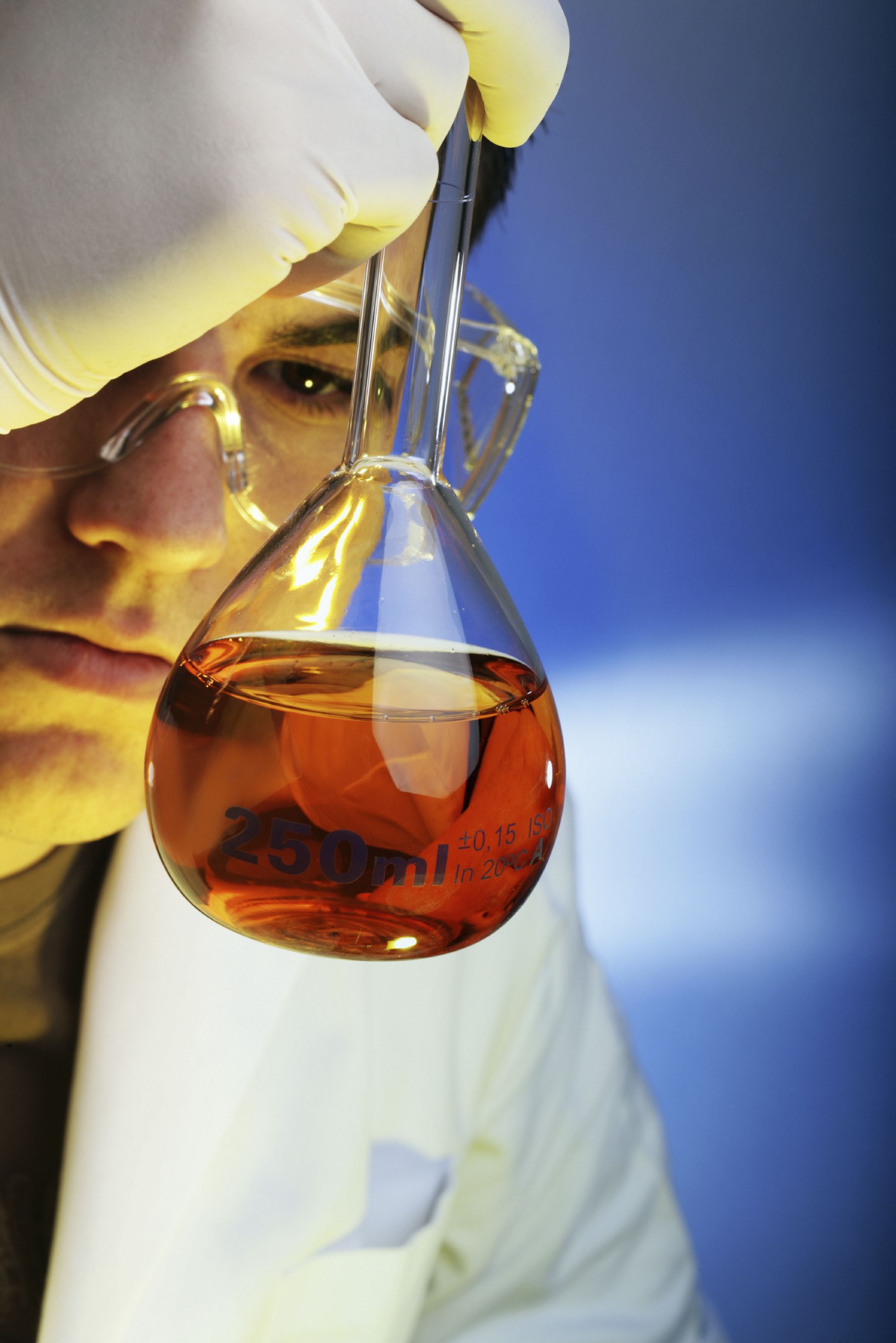 Scientist in safety glasses and gloves looking contents of beaker.